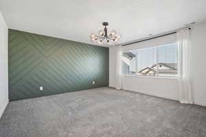 Carpeted spare room with wood walls, a textured ceiling, and a chandelier