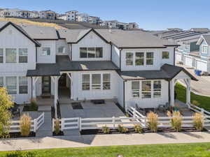 Modern inspired farmhouse featuring a residential view, board and batten siding, roof with shingles, a fenced front yard, and a patio area