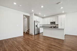 Kitchen with dark countertops, dark wood-style floors, appliances with stainless steel finishes, white cabinetry, and recessed lighting