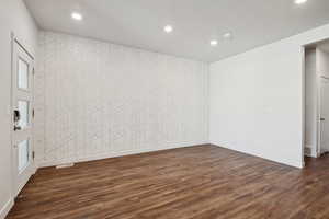 Unfurnished room with a textured ceiling, an accent wall, dark wood-type flooring, and recessed lighting