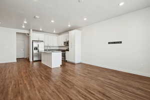 Kitchen with open floor plan, appliances with stainless steel finishes, dark wood-type flooring, a center island with sink, and white cabinets