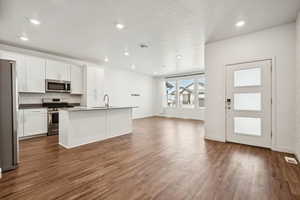 Kitchen featuring stainless steel appliances, a textured ceiling, dark wood finished floors, open floor plan, and white cabinetry