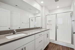 Full bathroom with double vanity, a shower stall, and wood finished floors