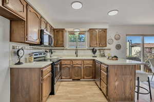 Kitchen featuring a peninsula, appliances with stainless steel finishes, a kitchen bar, light wood finished floors, and light countertops