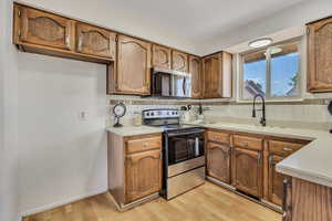 Kitchen featuring appliances with stainless steel finishes, light countertops, light wood finished floors, and brown cabinetry