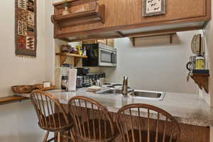 Kitchen featuring open shelves, stainless steel microwave, electric range oven, a kitchen bar, and brown cabinetry