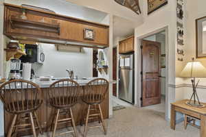 Kitchen with stainless steel appliances, a kitchen bar, brown cabinetry, light colored carpet, and a peninsula