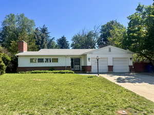 Ranch-style home with brick siding, a garage, concrete driveway, a front lawn, and a chimney