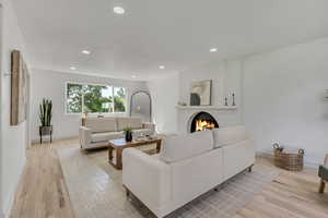 Living area with recessed lighting, a warm lit fireplace, and light wood-type flooring