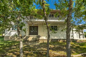 View of front of house featuring a balcony, french doors, brick siding, and a front lawn