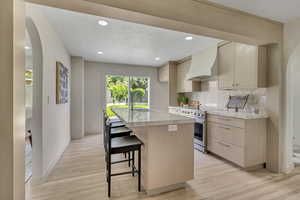Kitchen featuring arched walkways, premium range hood, light wood-type flooring, and recessed lighting