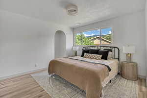 Bedroom featuring a textured ceiling, light wood-type flooring, and arched walkways