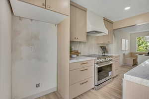 Kitchen featuring high end stainless steel range, custom range hood, light wood finished floors, recessed lighting, and decorative backsplash