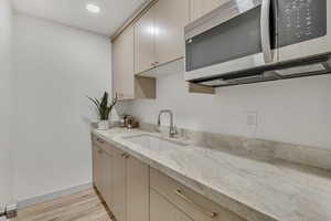 Kitchen featuring stainless steel microwave, light stone counters, light wood finished floors, and recessed lighting