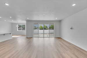 Unfurnished living room featuring light wood finished floors, recessed lighting, a textured ceiling, and a chandelier