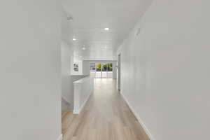Hallway with light wood-type flooring, an upstairs landing, and recessed lighting