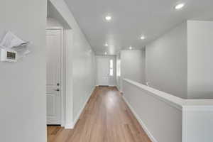 Corridor featuring light wood-style flooring, a textured ceiling, and recessed lighting