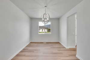 Unfurnished dining area featuring a chandelier, light wood-type flooring, and a textured ceiling