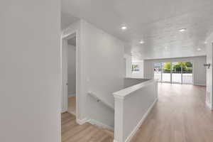 Hallway featuring an upstairs landing, light wood-style flooring, a textured ceiling, and recessed lighting