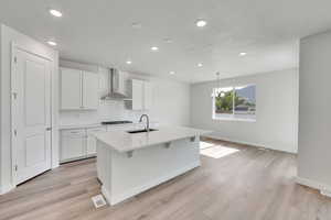 Kitchen featuring a kitchen island with sink, tasteful backsplash, light countertops, white cabinetry, and recessed lighting