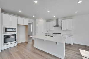 Kitchen with stainless steel oven, white cabinets, a center island with sink, light countertops, and built in microwave