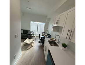Kitchen featuring dark wood-type flooring, white cabinets, light stone counters, and dishwasher