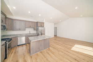 Kitchen featuring appliances with stainless steel finishes, a kitchen island, vaulted ceiling, recessed lighting, and light stone countertops
