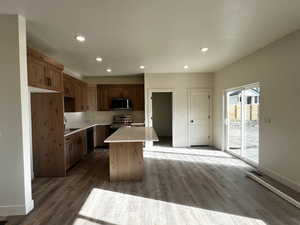 Kitchen featuring recessed lighting, stainless steel appliances, a kitchen island, dark wood-style floors, and brown cabinets