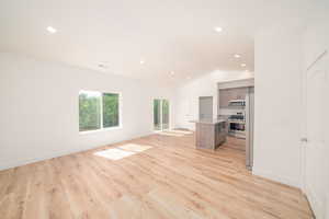 Unfurnished living room featuring vaulted ceiling, light wood-style flooring, and recessed lighting