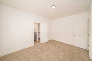 Unfurnished bedroom featuring light colored carpet and a walk in closet
