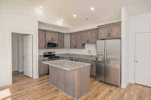 Kitchen featuring appliances with stainless steel finishes, lofted ceiling, a kitchen island, light stone countertops, and light wood-type flooring
