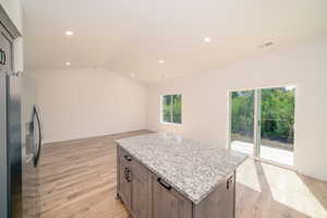 Kitchen with lofted ceiling, stainless steel fridge with ice dispenser, light wood-type flooring, light stone counters, and recessed lighting