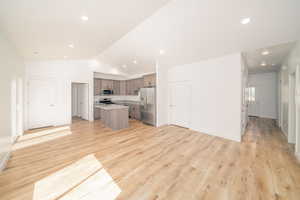 Kitchen with a kitchen island, open floor plan, stainless steel appliances, vaulted ceiling, and light wood finished floors