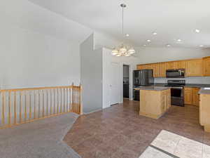 Kitchen featuring vaulted ceiling, stainless steel appliances, a chandelier, a kitchen island, and light brown cabinetry