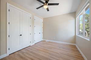Unfurnished bedroom with light wood finished floors, multiple closets, and ceiling fan