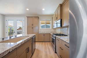 Kitchen featuring appliances with stainless steel finishes, healthy amount of natural light, a textured ceiling, light wood finished floors, and recessed lighting
