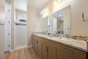 Full bathroom featuring double vanity, wood finished floors, and a tile shower