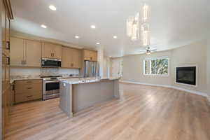 Kitchen featuring stainless steel appliances, a center island with sink, a glass covered fireplace, recessed lighting, and open floor plan
