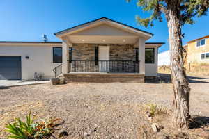 View of front facade featuring an attached garage, a porch, stucco siding, and stone siding