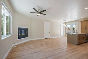 Unfurnished living room featuring light wood finished floors, a textured ceiling, a glass covered fireplace, a ceiling fan, and recessed lighting