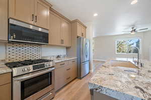 Kitchen featuring stainless steel appliances, light wood-type flooring, ceiling fan, light stone counters, and recessed lighting