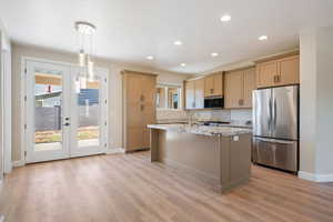 Kitchen featuring appliances with stainless steel finishes, an island with sink, french doors, light stone counters, and recessed lighting