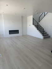 Unfurnished living room with stairs, light wood-type flooring, and a glass covered fireplace