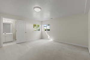Unfurnished bedroom with a textured ceiling, light colored carpet, and ensuite bathroom