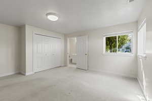 Unfurnished bedroom featuring a textured ceiling, light colored carpet, a closet, and ensuite bath