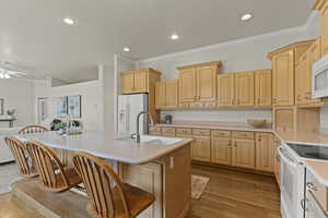 Kitchen with crown molding, light brown cabinetry, light countertops, white appliances, and light wood finished floors