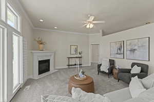Living room with carpet flooring, ornamental molding, a high end fireplace, ceiling fan, and recessed lighting