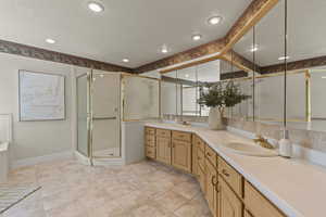 Bathroom with a textured ceiling, double vanity, a shower stall, light tile patterned flooring, and recessed lighting