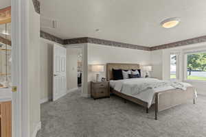 Bedroom featuring a textured ceiling, light colored carpet, and attic access