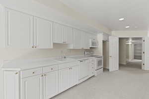Kitchen featuring white appliances, white cabinets, light colored carpet, light countertops, and recessed lighting